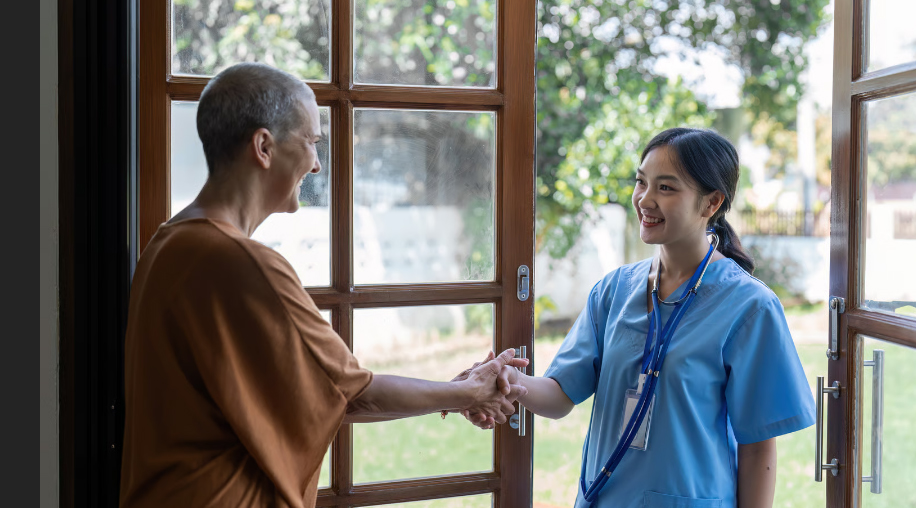 A smiling James River Home Health nurse in blue scrubs shaking hands with a senior patient at her front door in Virginia.